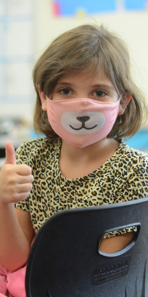Elementary student wearing a mask and holding a thumbs up Elementary student wearing a mask and holding a thumbs up